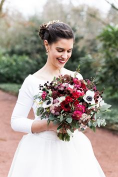 a woman in a white dress holding a bouquet of red and white flowers on her wedding day