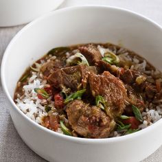 a white bowl filled with rice and meat on top of a table next to a cup