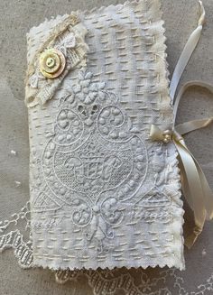 an old book with lace and ribbon on the cover is sitting on a tablecloth