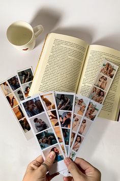 a person holding several photos in front of an open book on a table with a cup and saucer