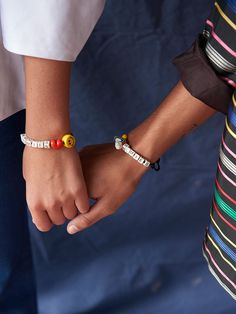 two people are holding hands with bracelets on their wrists and one is wearing a striped shirt