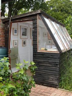 a small wooden shed with a glass roof and windows on the side, in front of some trees