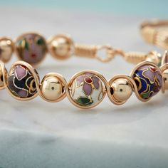 Each cloisonné bead is inlaid with colored enamel, giving the beads a dainty, feminine look. Adjustable Fusion Jewelry With Polished Beads, Metal Bracelets With Spacer Beads For Gift, Spiritual Bracelets With Colorful Beads, Hand Painted Gold Metal Jewelry, Hand Painted Gold Bracelet, Adjustable Gold Enamel Bracelets, Rose Gold Metal Bracelets With Round Beads, Rose Gold Metal Bracelet With Round Beads, Gold Hand Painted Bracelets As Gift