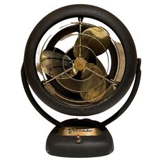 an old fashioned fan sitting on top of a black stand next to a white wall