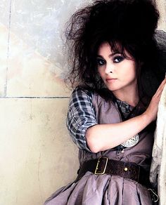 a woman leaning against a wall with her hair blowing in the wind and wearing a dress