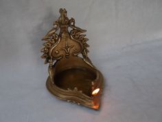 an ornate brass candle holder with a lit candle in the center on a white background