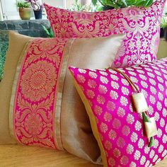 three pink and gold pillows sitting on top of a wooden table next to a potted plant