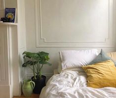 a bed with white sheets and yellow pillows in a room next to a plant on the floor