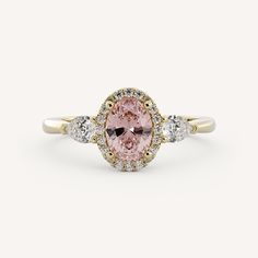 a pink diamond ring with three white diamonds on the band and an oval shaped center stone