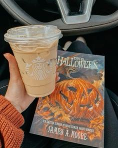 a person holding a cup of coffee and a book in their hand while sitting in a car