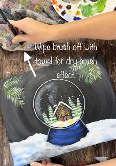 two hands are painting a snow globe on a piece of wood that says, wipe brush off with towel for drybrush effect