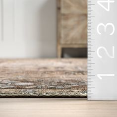 a large ruler is on the floor next to a dresser with drawers and an area rug