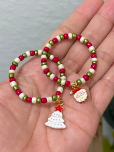 a hand holding two bracelets with beads and charms on each one, including a christmas tree ornament