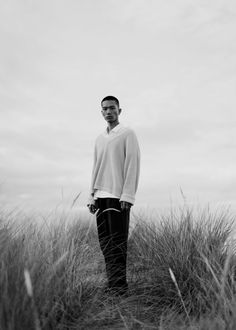 a black and white photo of a man standing in tall grass with his hands in his pockets