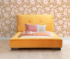 an orange bed with pillows on it in front of a wallpapered background and wooden floor