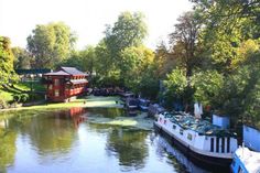 boats are docked on the river in front of a red building and some green trees