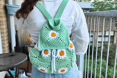 a woman wearing a green crocheted backpack with flowers on the front and side