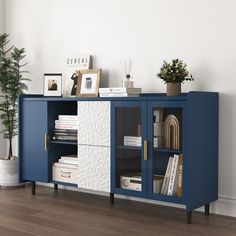 a blue and white sideboard with books on it in a room next to a potted plant