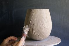 a person is painting a vase on a table