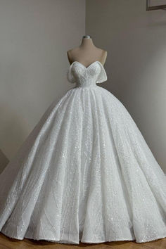 a white ball gown on a mannequin stand in front of a wall and window