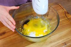 someone mixing eggs in a glass bowl on a wooden cutting board