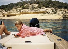 a young boy laying on top of a boat next to another person holding a cell phone