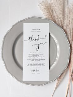 a wedding thank card sitting on top of a plate next to some dry grass and flowers