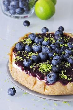 a cake with blueberries and limes on the side sitting on a white table