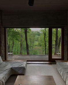 two beds in a room with large windows overlooking the woods and trees, next to each other