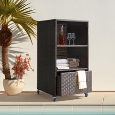 a brown wicker cabinet next to a potted plant with wine glasses on it