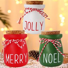 three mason jars with merry and noel painted on them sitting on a table next to pine cones