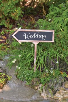 a wooden sign that says wedding next to some water and plants in the background with flowers