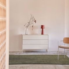 a white dresser sitting next to a red vase on top of a wooden table in a living room