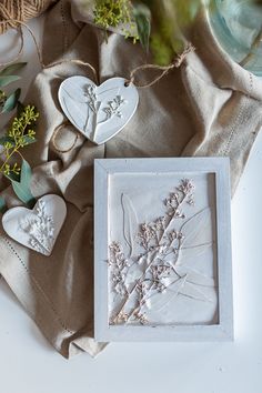 two white heart shaped ornaments sitting on top of a table next to some flowers and twine