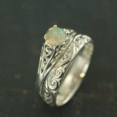 a white gold ring with an opal stone in the center and filigrees around it