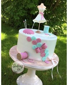 a white cake with pink and blue buttons on it sitting in the middle of grass