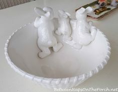 two white ceramic figurines in a bowl on a table next to a magazine