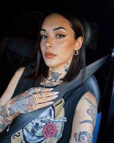 a woman with tattoos on her arm and chest sitting in the back seat of a car