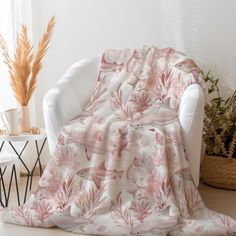 a white chair sitting next to a window covered in a pink flowered throw blanket