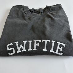 "My absolute favorite tee! Wear it loud and proud; this comfort colors \"SWIFTIE\" tee can be customized with your fave thread color.  Please wash on gentle cycle and dry on low.  If you are wanting a different design, wording, or a different clothing style, please send me a message so we can discuss the details. Please include thread color at checkout" Soft-washed Cotton Crew T-shirt, Collegiate Embroidered Crew Neck T-shirts, Collegiate Cotton T-shirt With Embroidered Graphics, Cotton College T-shirt With Embroidered Graphics, Cotton Crew T-shirt With Embroidered Graphics, Gray Cotton T-shirt With School Spirit, College T-shirt With Embroidered Graphics And Relaxed Fit, Cotton Tops With Embroidered Graphics For Sports Events, Relaxed Fit Crew T-shirt For College