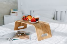 a bed with a tray of fruit on top of it and a magazine next to it