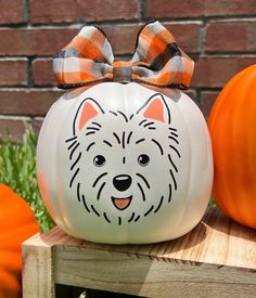 a white pumpkin with a dog's face painted on it and a bow around its head