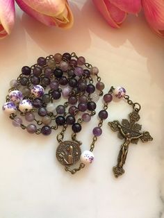 "Handmade bronze St. Teresa of Avila rosary made with 6mm purple amethyst gemstone beads and 8mm purple & white floral ceramic beads. The vintage inspired bronze Saint Teresa center measures 13/16\". The crucifix measures approximately 1 3/4\"." Lavender Spiritual Jewelry With 8mm Beads, Spiritual Lavender Jewelry With 8mm Beads, Lavender Spiritual Jewelry With Beads, Purple Rosary With 8mm Beads, Purple Rosary With 8mm Round Beads, Handmade Adjustable Purple Rosary, Handmade Spiritual Purple Rosary Bracelet, Beautiful Rosaries, St Teresa Of Avila