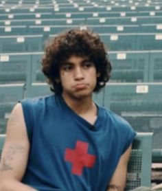 a young man sitting in the bleachers with his hands on his hips and wearing a red cross t - shirt