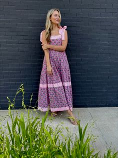 This is it! THE dress of the summer! Meet Maisie, our newest cotton block print maxi dress in a Pink Posey print. She’s full of sweet details like a tiered skirt, and contrasting striped banding. The bow straps are adjustable for the perfect fit, and it features a smocked back panel for comfort. Did we mention it has POCKETS!? Whether you're sipping lemonade on the porch or hitting up a summer wedding or soirée, this dress is a fun, versatile addition to your closet. Throw it on with sneakers or Cotton Tiered Dress For Vacation, Cotton Dress With Tie Straps And Tiered Skirt, Cotton Tiered Skirt Maxi Dress For Garden Party, Cotton Tiered Maxi Dress For Garden Party, Cotton Maxi Dress With Tiered Skirt For Garden Party, Cotton Tiered Dress For Garden Party, Spring Cotton Tiered Maxi Dress, Tiered Cotton Maxi Dress For Garden Party, Casual Cotton Maxi Tiered Dress