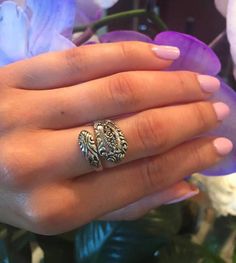 a woman's hand with a ring on it and purple flowers in the background