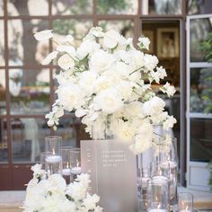 white flowers and candles are arranged on a table in front of a glass building with windows