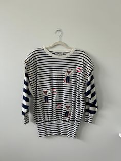 Super unique top or tunic with a combination of stripes and nautical sailor embroidered figures. Grommets along the shoulders. Tag says 1X but fits smaller. This could be great on with linen pants or as a beach sweater. Cotton Sailor Style Top, White Vertical Stripes Top For Vacation, Marine Style Cotton Crew Neck Top, White Sailor Style Long Sleeve Tops, Striped Crew Neck Tops For Vacation, Casual Oversized Top With Striped Cuffs, Navy Sailor Crew Neck Top, Casual Tops With Striped Collar For Vacation, Casual Top With Striped Collar For Vacation