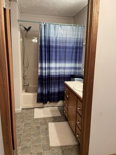 a bathroom with a blue shower curtain next to a white sink and brown wooden cabinets