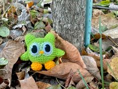 an owl stuffed animal sitting on top of leaves next to a tree in the woods